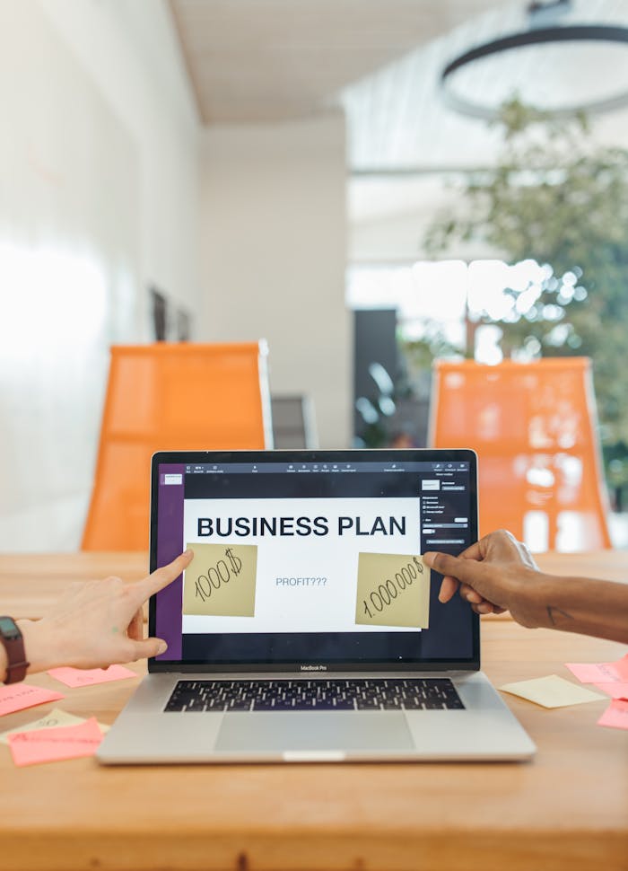 Hands pointing at business plan on laptop screen in modern office.